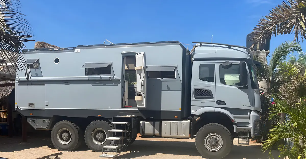 A grey luxury 6x6 overland expedition RV truck parked at a tropical camper resort near Huatulco